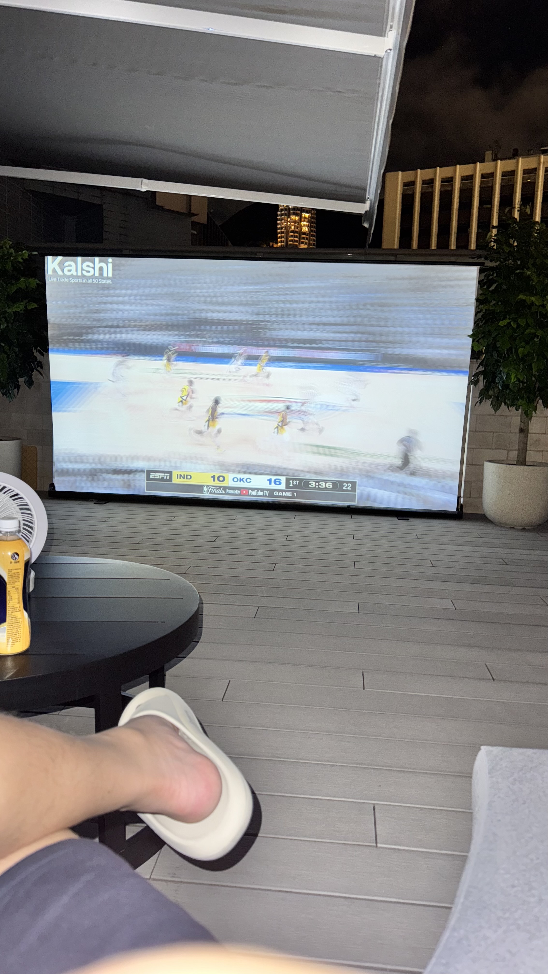 A person relaxing on a patio with feet up, watching a sports game projected on a screen