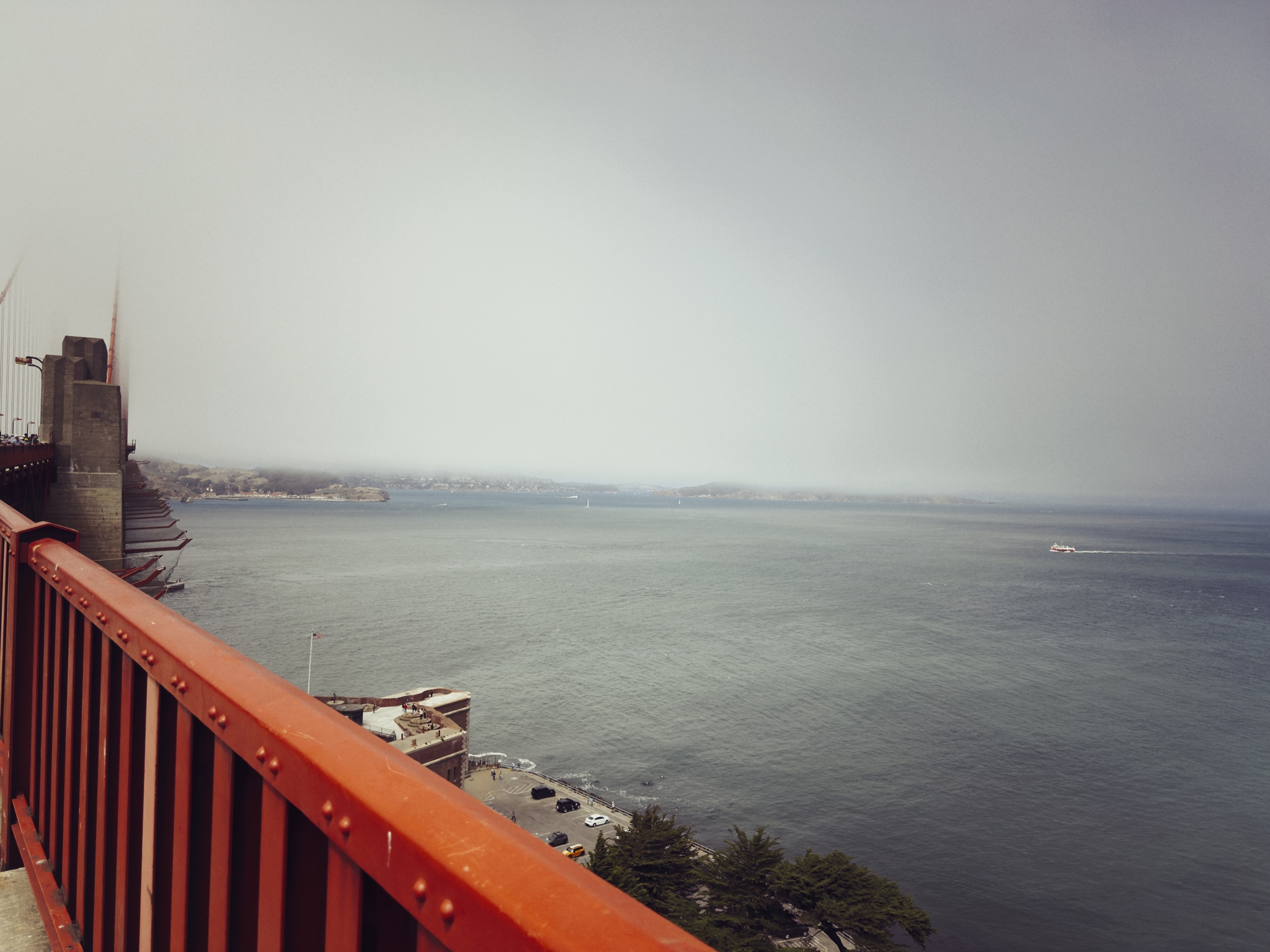 A view from a red bridge railing overlooking a calm body of water with a hazy sky and distant shoreline
