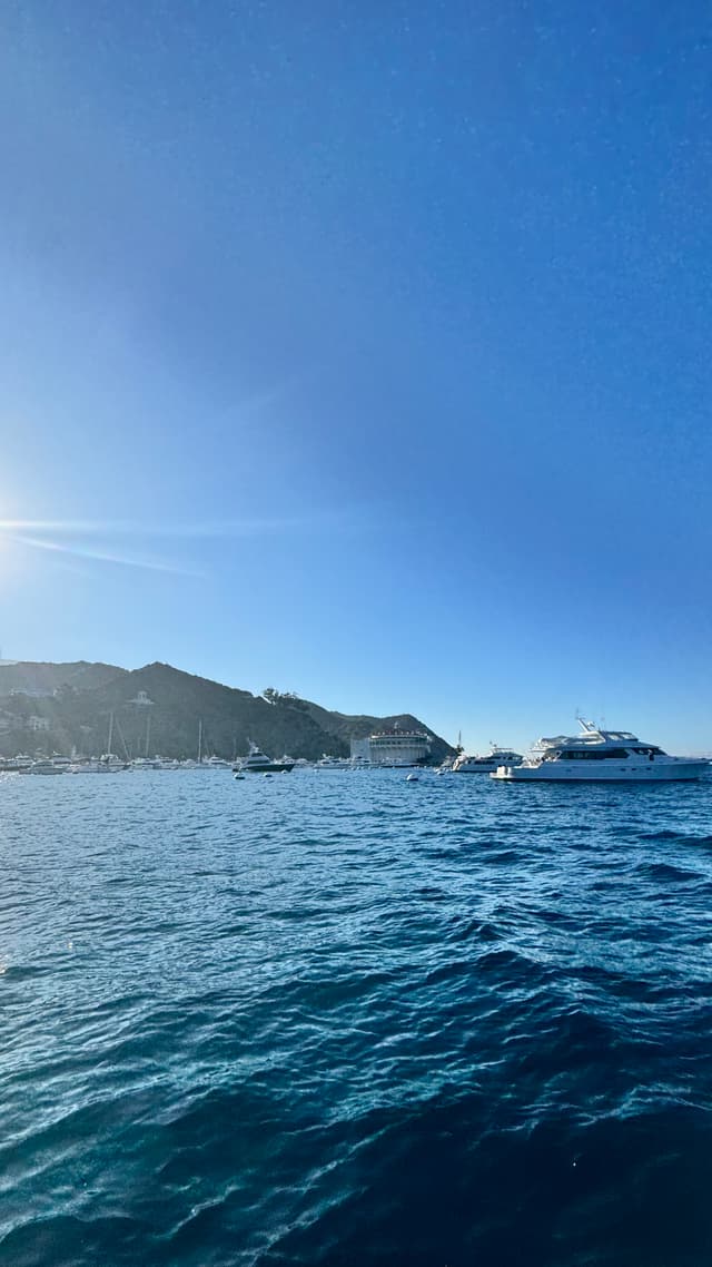 A serene ocean scene with a clear blue sky, boats on the water, and a distant coastline
