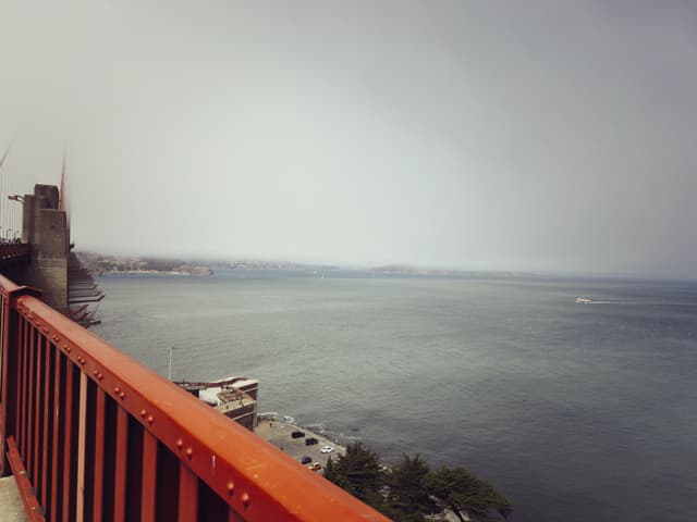 A view from a red bridge railing overlooking a calm body of water with a hazy sky and distant shoreline