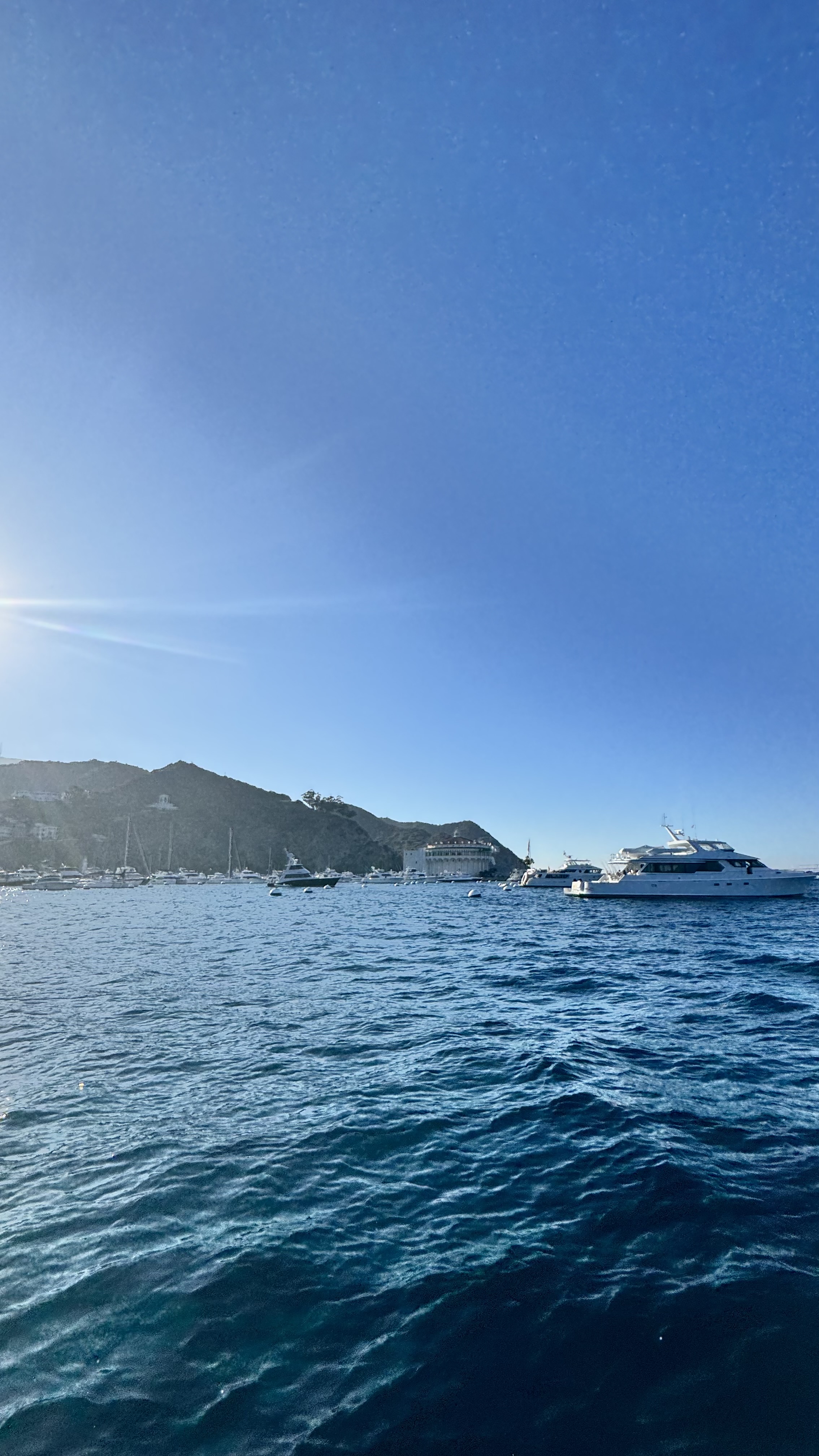 A serene ocean scene with a clear blue sky, boats on the water, and a distant coastline